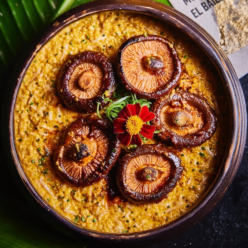 Creamy golden grain dish topped with roasted shiitake mushrooms, herbs, and a red edible flower in a rustic bowl.