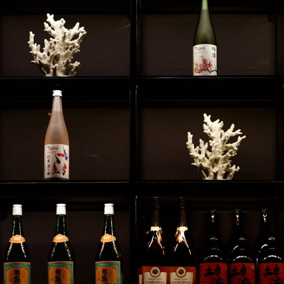 Japanese sake and wine bottles displayed among coral-like white sculptures on dark wooden shelves.